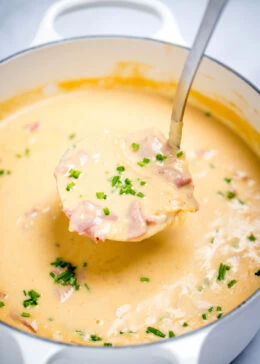 A ladle scooping reuben soup topped with chives out of a dutch oven.