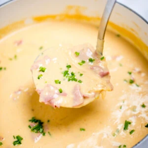 A ladle scooping reuben soup topped with chives out of a dutch oven.