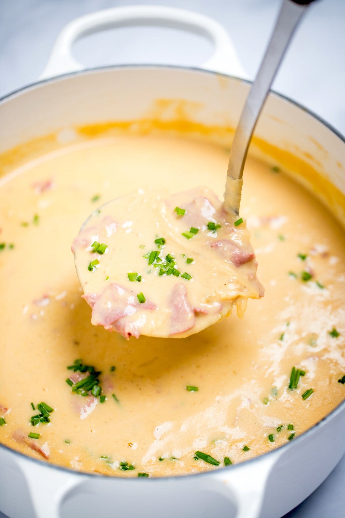 A ladle scooping reuben soup topped with chives out of a dutch oven.