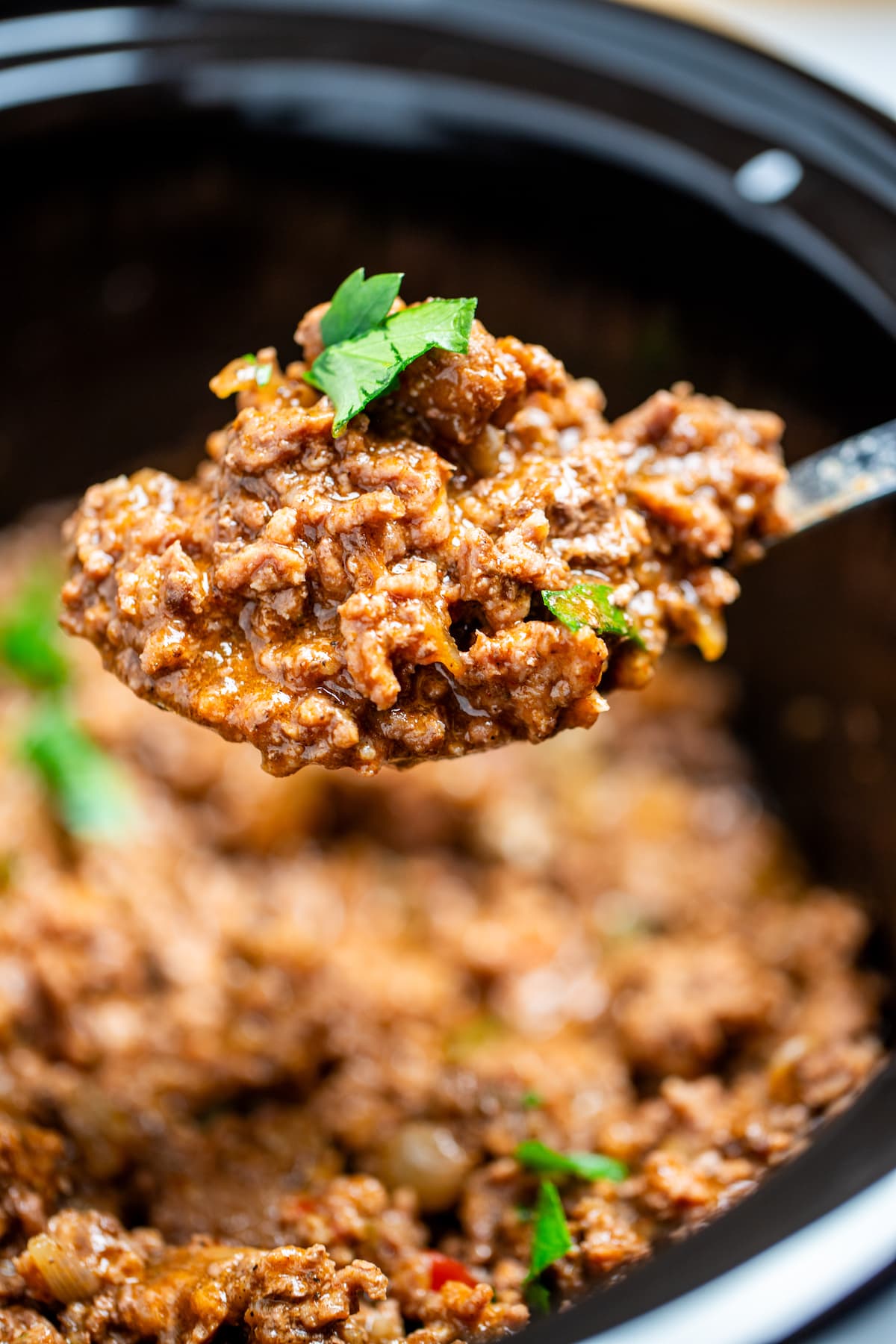 Slow cooker full of slow cooker taco meat topped with fresh parsley, with a spoon scooping meat up.
