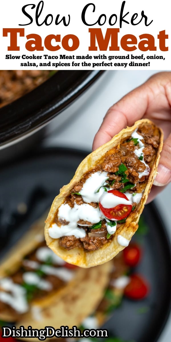 Pinterest pin with a hand holding a beef taco drizzled with sour cream and cherry tomatoes above a plate of tacos, in front of a slow cooker full of slow cooker taco meat.