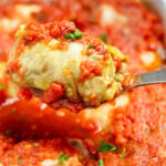 A spoon lifting a stuffed cabbage roll out of a baking dish.