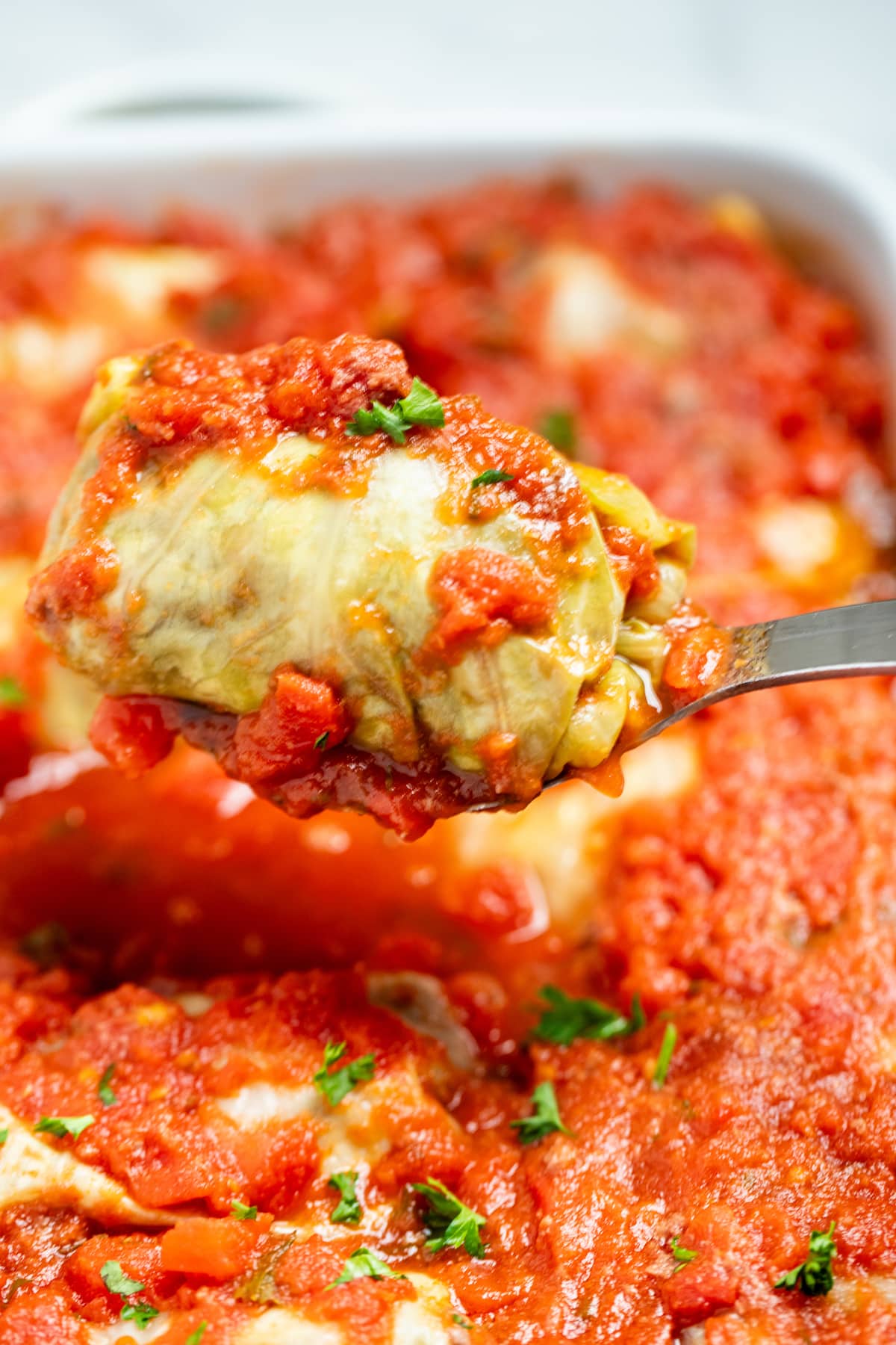 A spoon lifting a stuffed cabbage roll out of a baking dish.