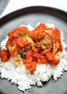 Stuffed cabbage rolls cut in half on top of rice on a plate, topped with more tomato sauce.