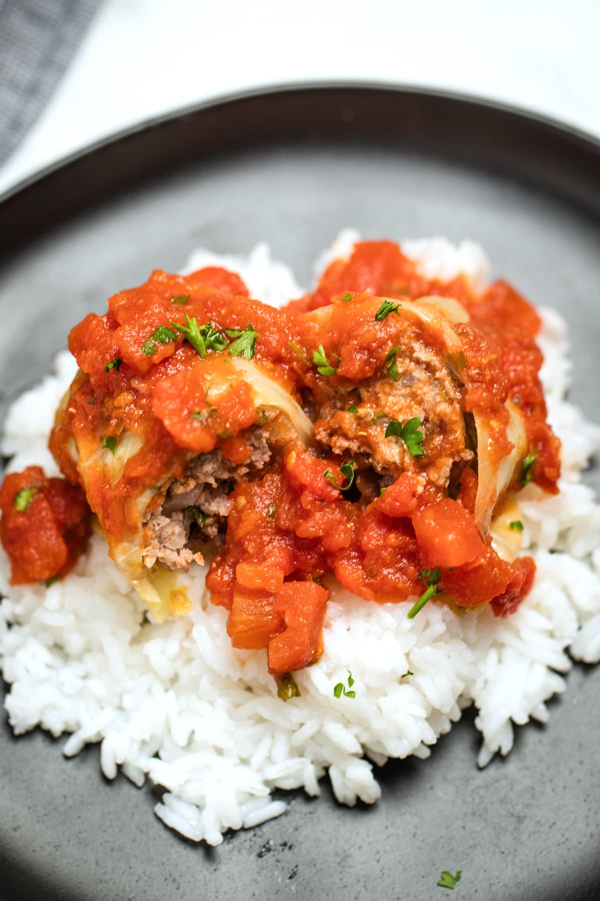 Stuffed cabbage rolls cut in half on top of rice on a plate, topped with more tomato sauce.