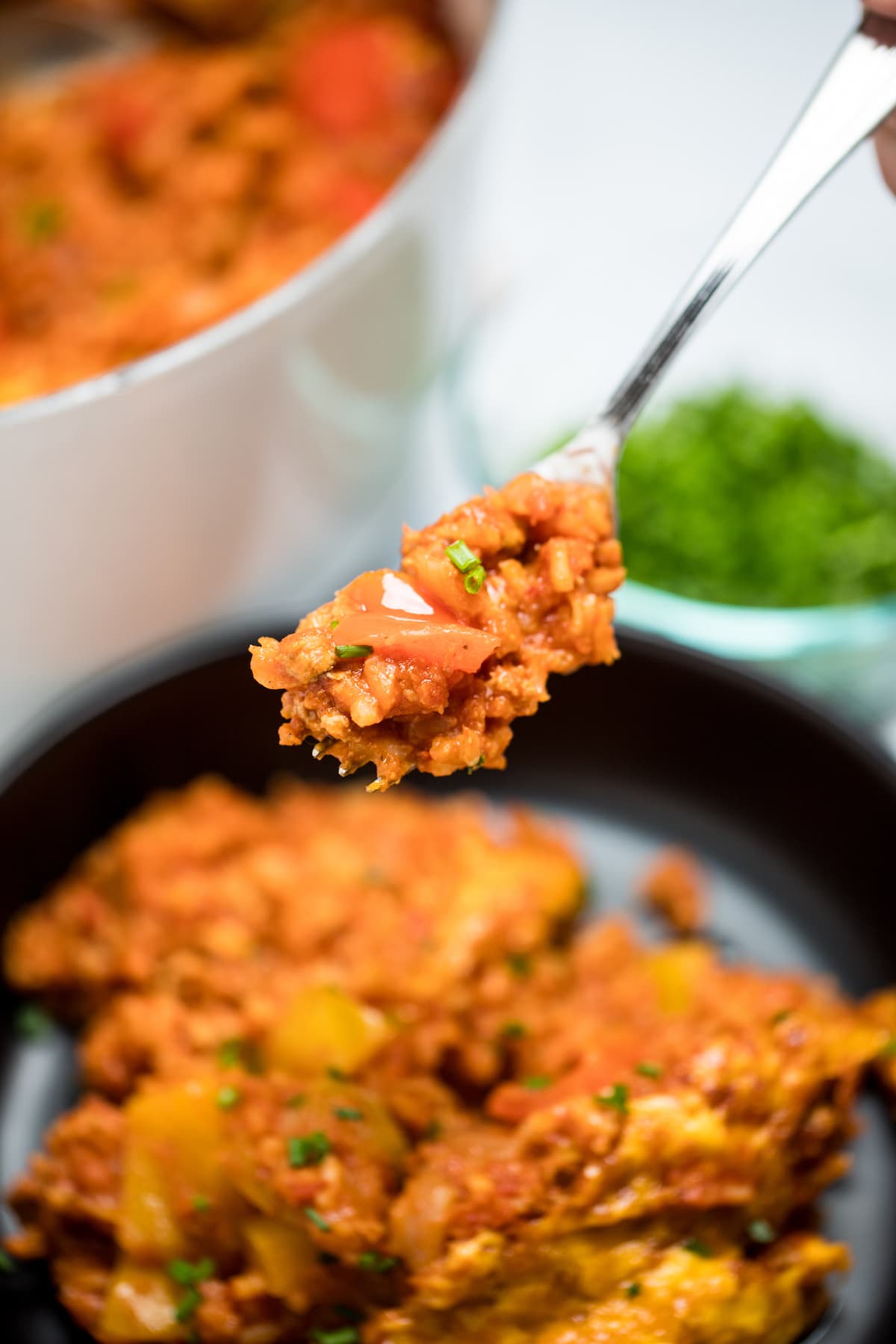 Stuffed pepper casserole on a plate with a fork holding some casserole, in front of a dutch oven and a small bowl of chopped chives.