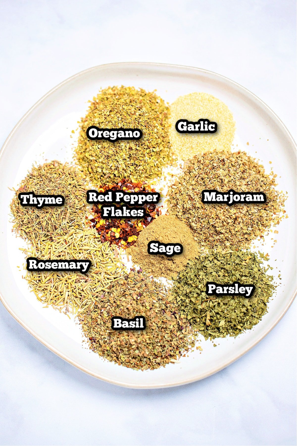 Individual ingredients for homemade Italian seasoning on a plate on a table.