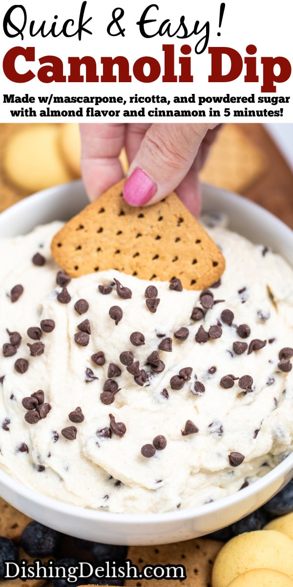 Pinterest pin with a bowl of cannoli dip topped with mini chocolate chips, with a hand using a graham cracker to scoop up some dip. The bowl is sitting on a cutting board surrounded by graham crackers, blueberries, and vanilla wafers.