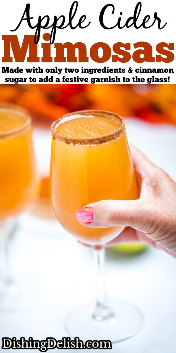 Pinterest pin with a hand holding a wine glass filled with apple cider mimosas, with another wine glass on a table in the background.