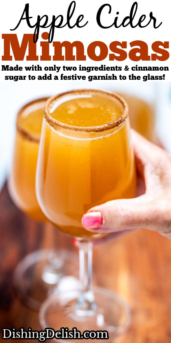 Pinterest pin with a hand holding a wine glass filled with apple cider mimosas, with another wine glass on a cutting board in the background.