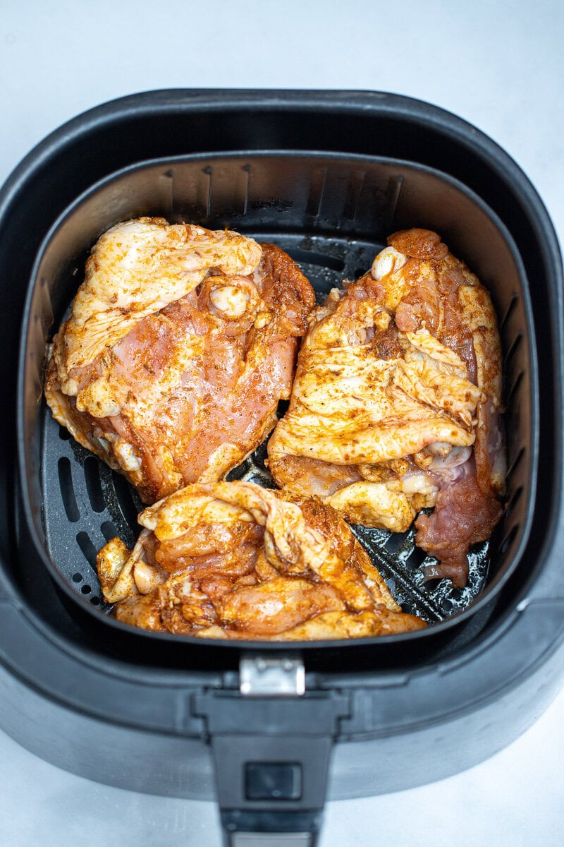 Raw seasoned chicken thighs in an air fryer basket.