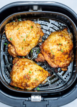Chicken thighs in an air fryer basket with chopped chives on top of crispy skin.