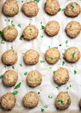 Baked turkey meatballs on a sheet pan lined with parchment paper, fully cooked and topped with fresh chopped parsley.