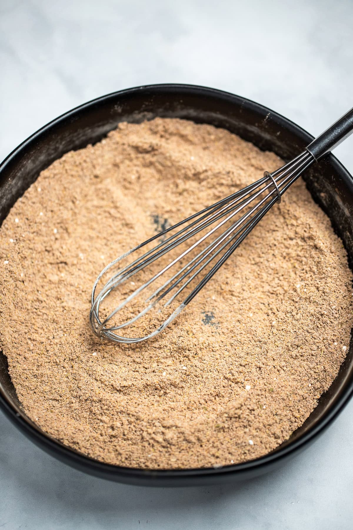 A bowl on a table with fajita seasoning mixed together, with a whisk resting in the bowl.