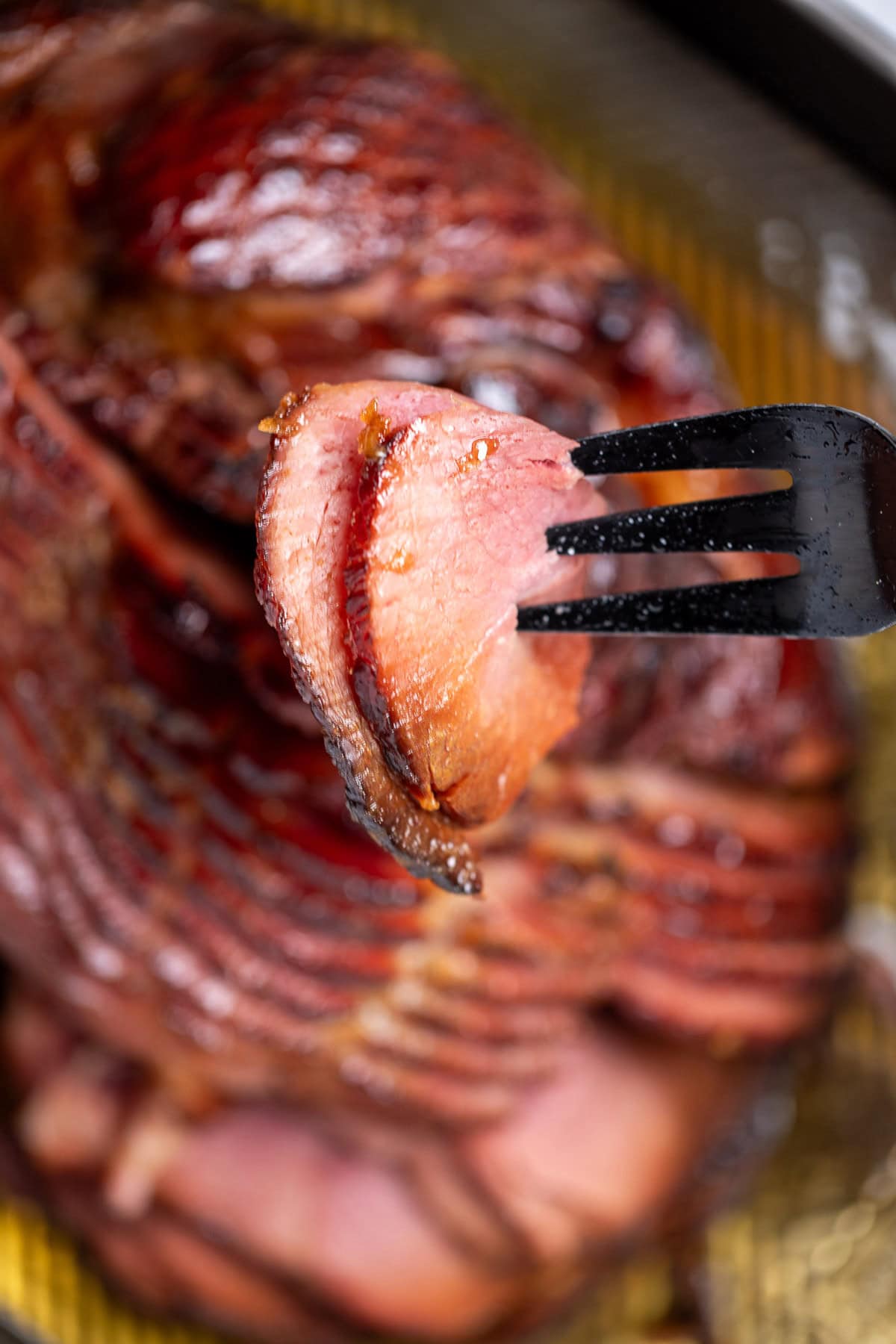 A fork lifting two pieces of ham over a spiral ham on a sheet pan.