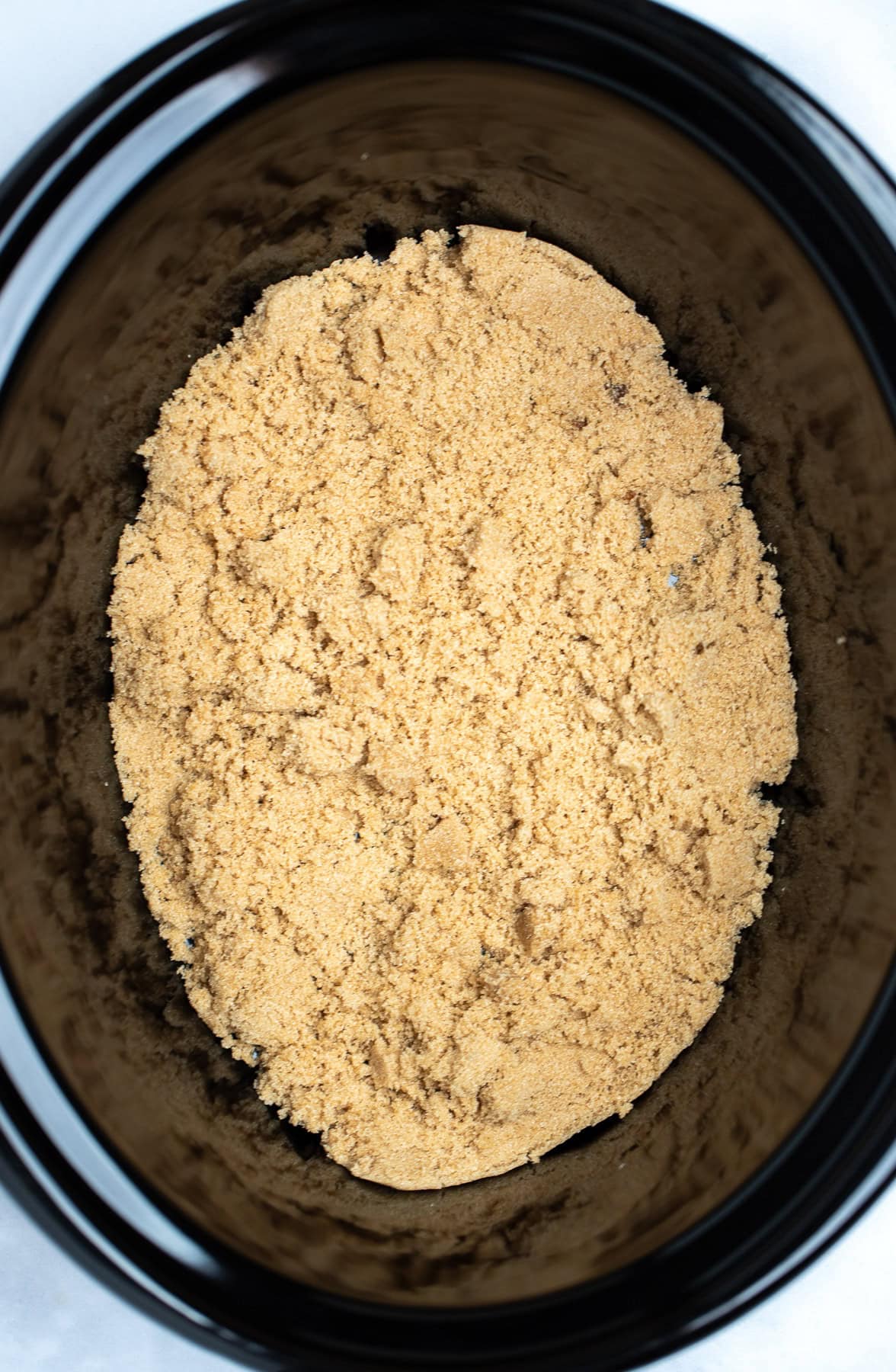A slow cooker pot with the bottom of the pot covered in brown sugar.