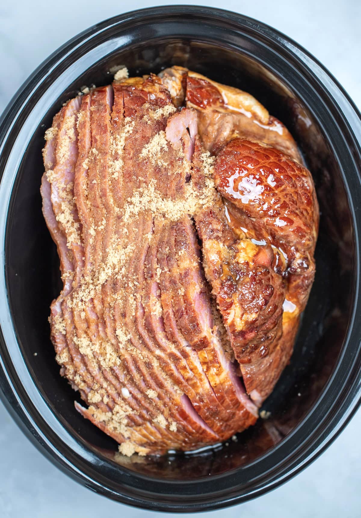 A slow cooker with a spiral ham on its side, topped with brown sugar and honey, before being slow cooked.