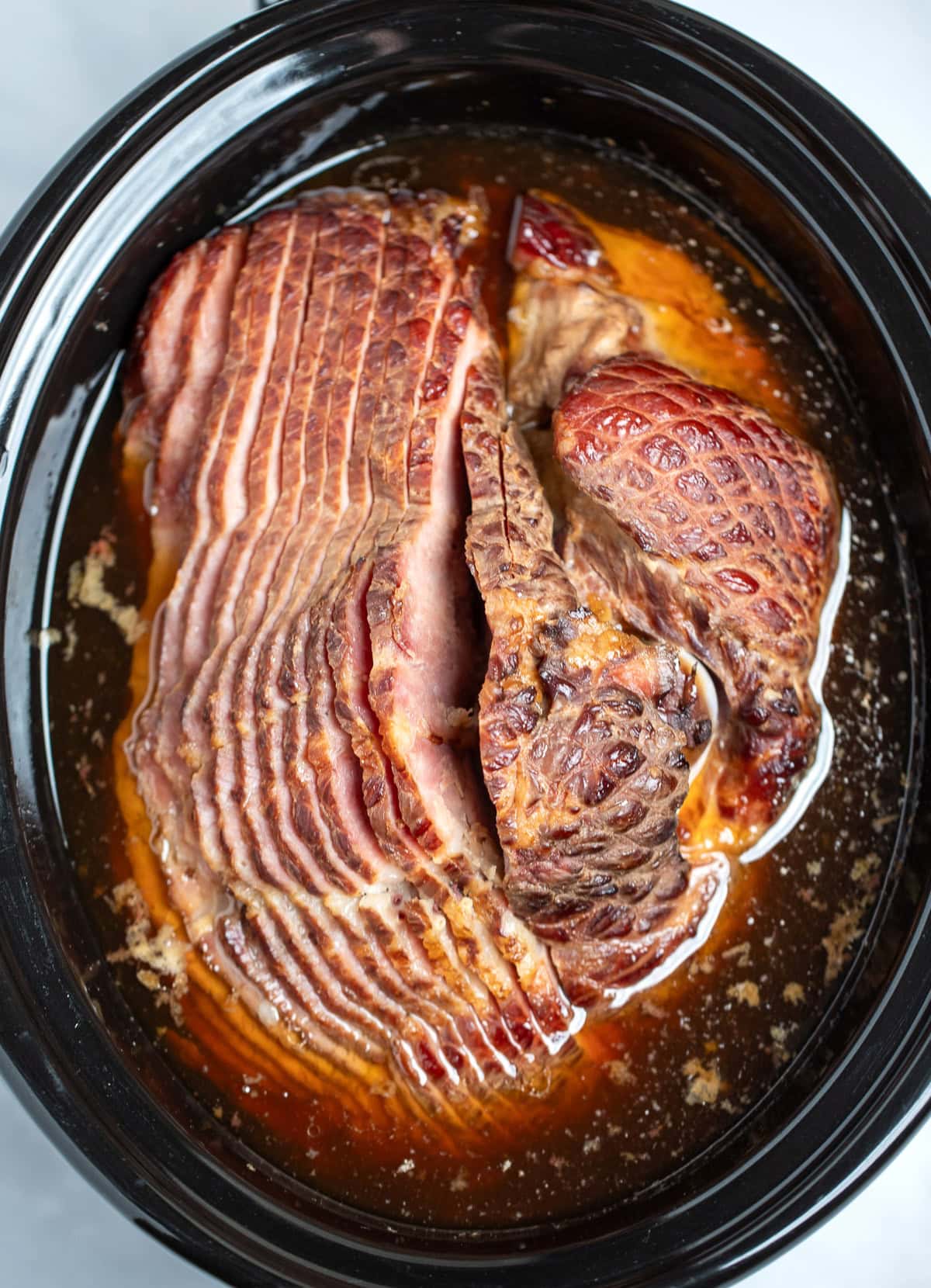 A slow cooker with a spiral ham on its side sitting in its cooking juices.