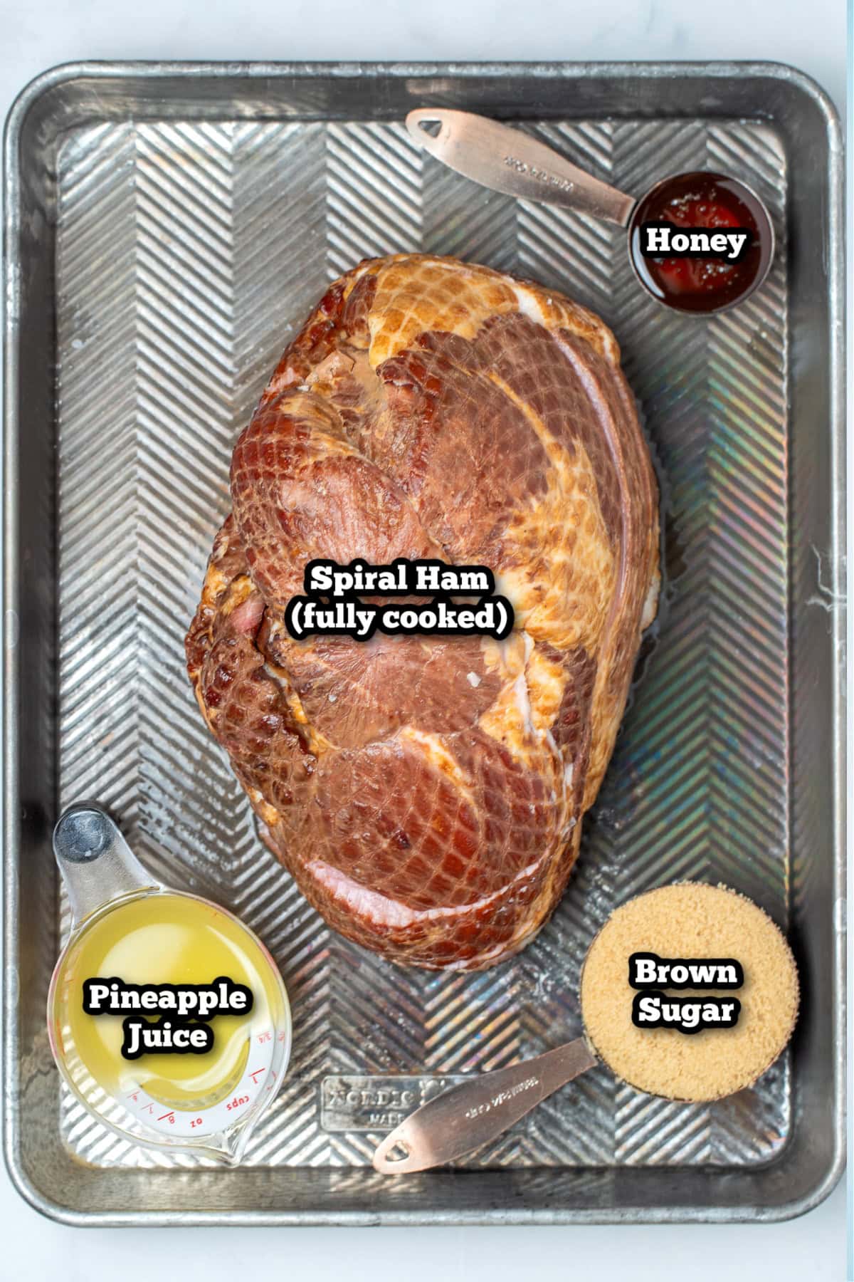 Individual ingredients for slow cooker spiral ham on a sheet pan on a table.
