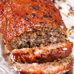 A meatloaf sitting on aluminum foil with two slices falling from the front of the loaf.