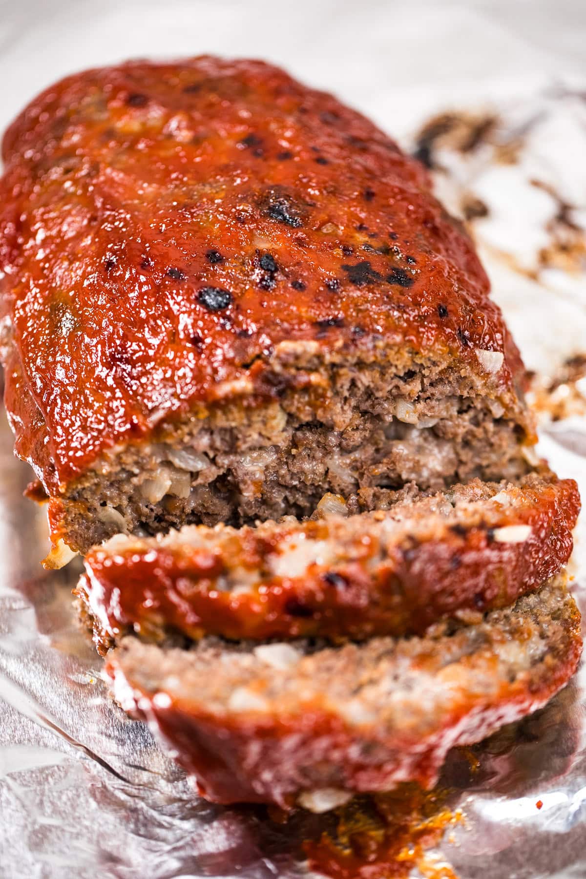 A meatloaf sitting on aluminum foil with two slices falling from the front of the loaf.