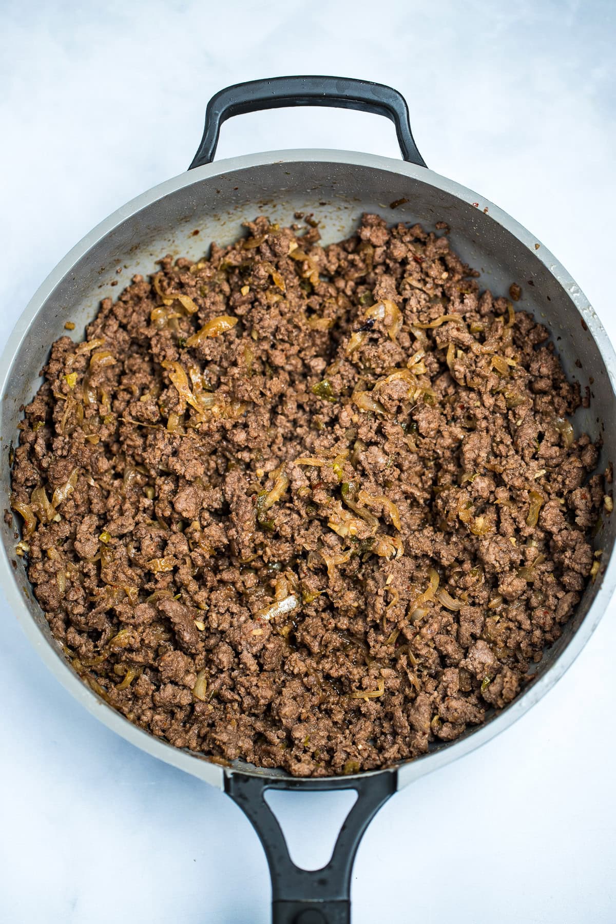A skillet of ground beef cooked with seasoning and onions.