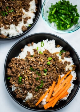 A pinterest pin with a bowl of rice topped with seasoned beef with raw carrot sticks and green onions, with another bowl and green onions in the background.
