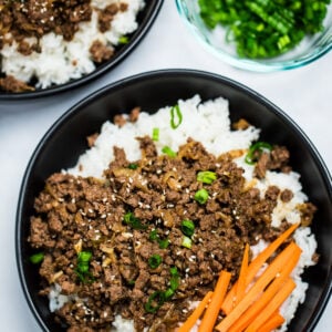 A pinterest pin with a bowl of rice topped with seasoned beef with raw carrot sticks and green onions, with another bowl and green onions in the background.