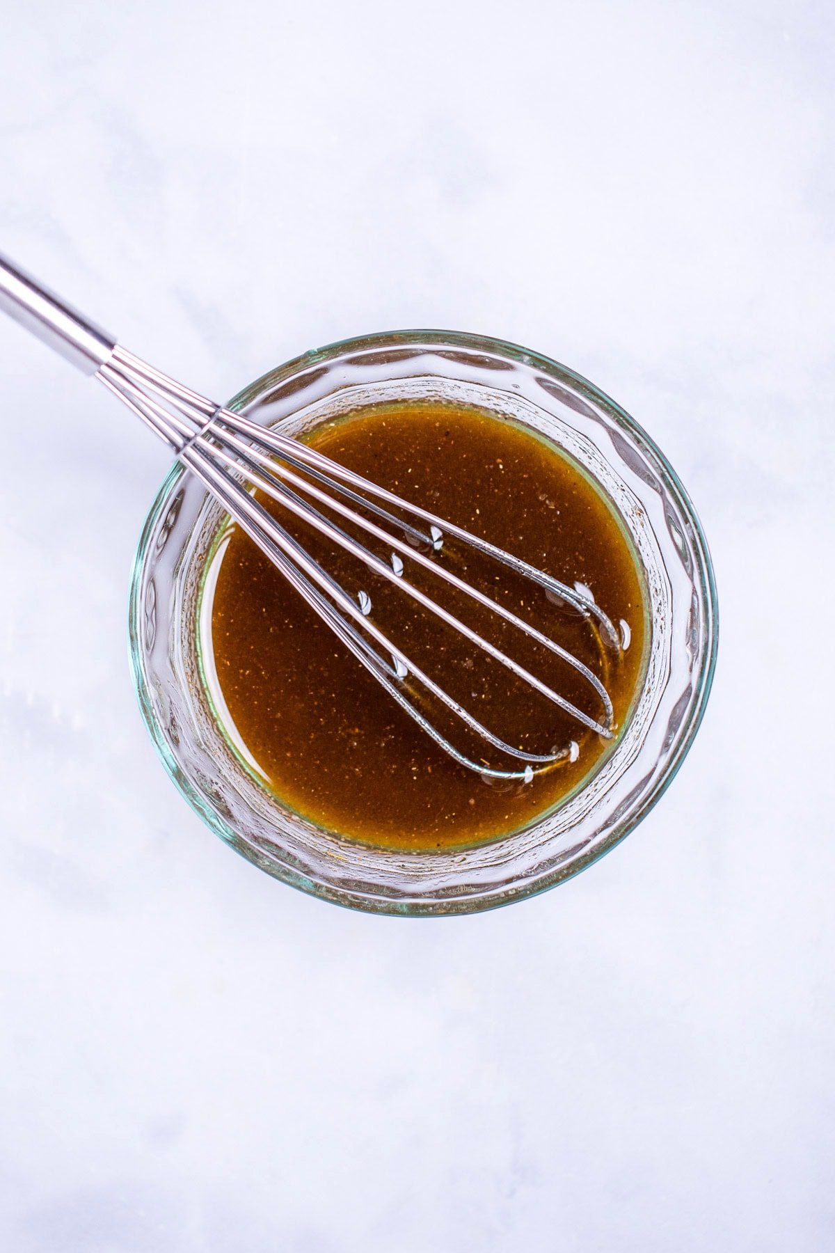 A small glass bowl with vinaigrette and a whisk having just mixed it together.