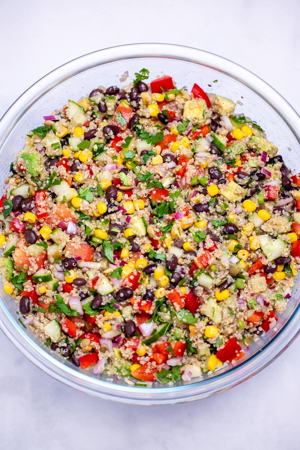 A glass bowl on a table with black bean quinoa salad in it topped with fresh chopped cilantro.