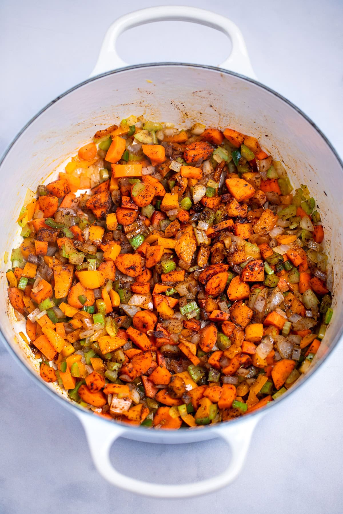 A dutch oven with sautéd vegetables, sitting on a table.