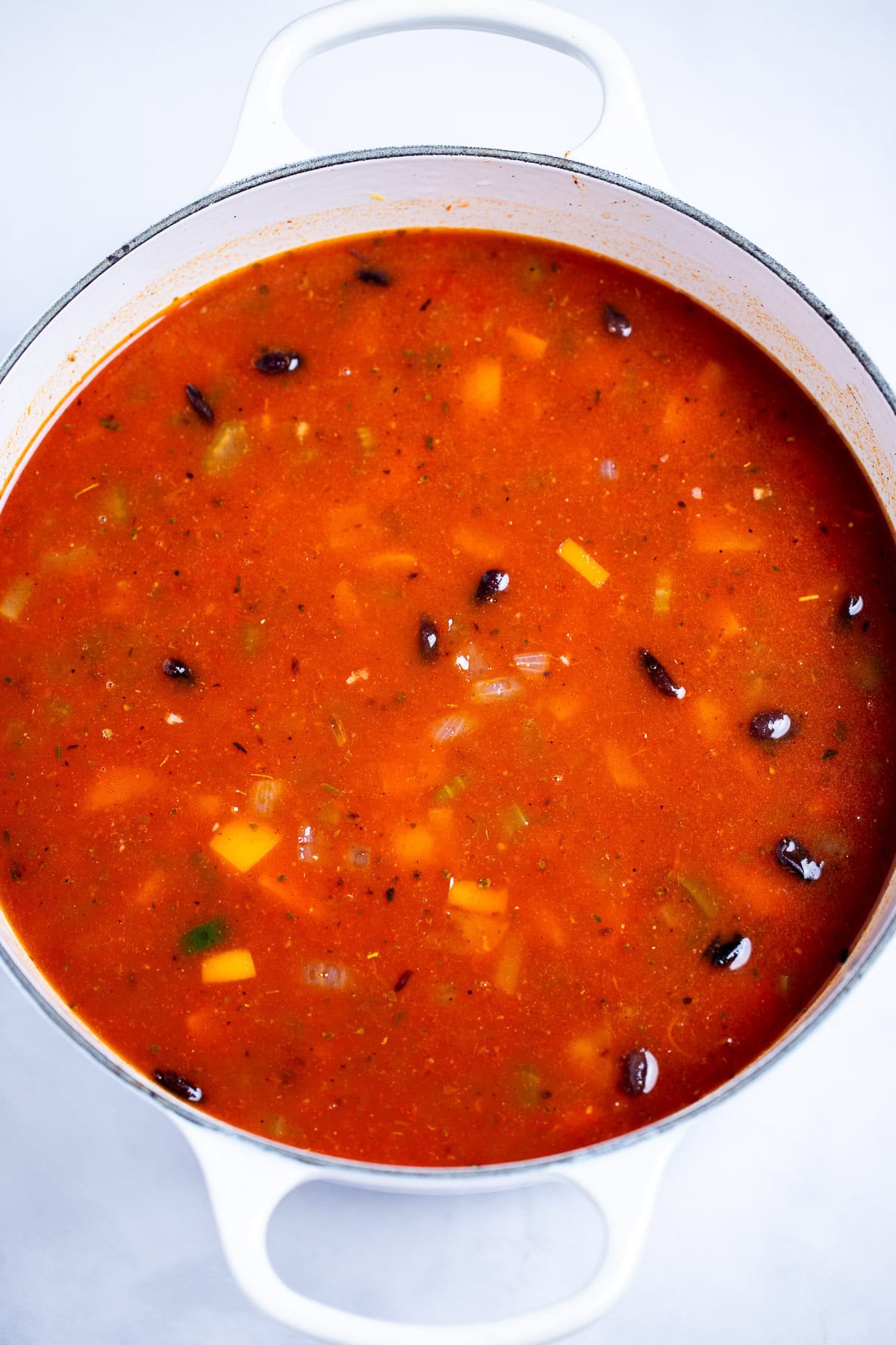 A dutch oven with black bean soup before being pureed, sitting on a table.