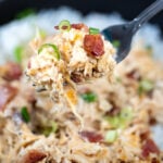 A fork lifting some cream cheese chicken up topped with crispy bacon pieces and green onion.