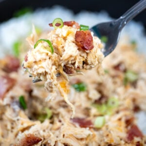 A fork lifting some cream cheese chicken up topped with crispy bacon pieces and green onion.