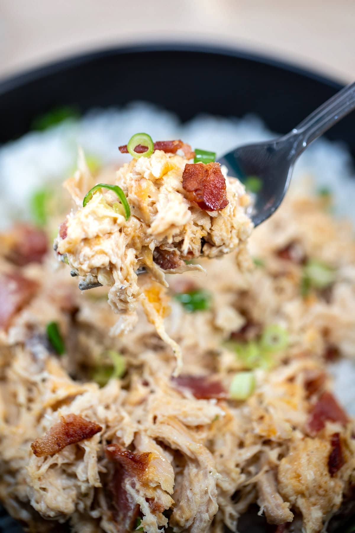 A fork lifting some cream cheese chicken up topped with crispy bacon pieces and green onion.