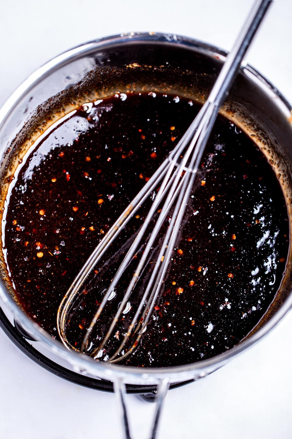 A saucepan with balsamic reduction in it with spices and a whisk.