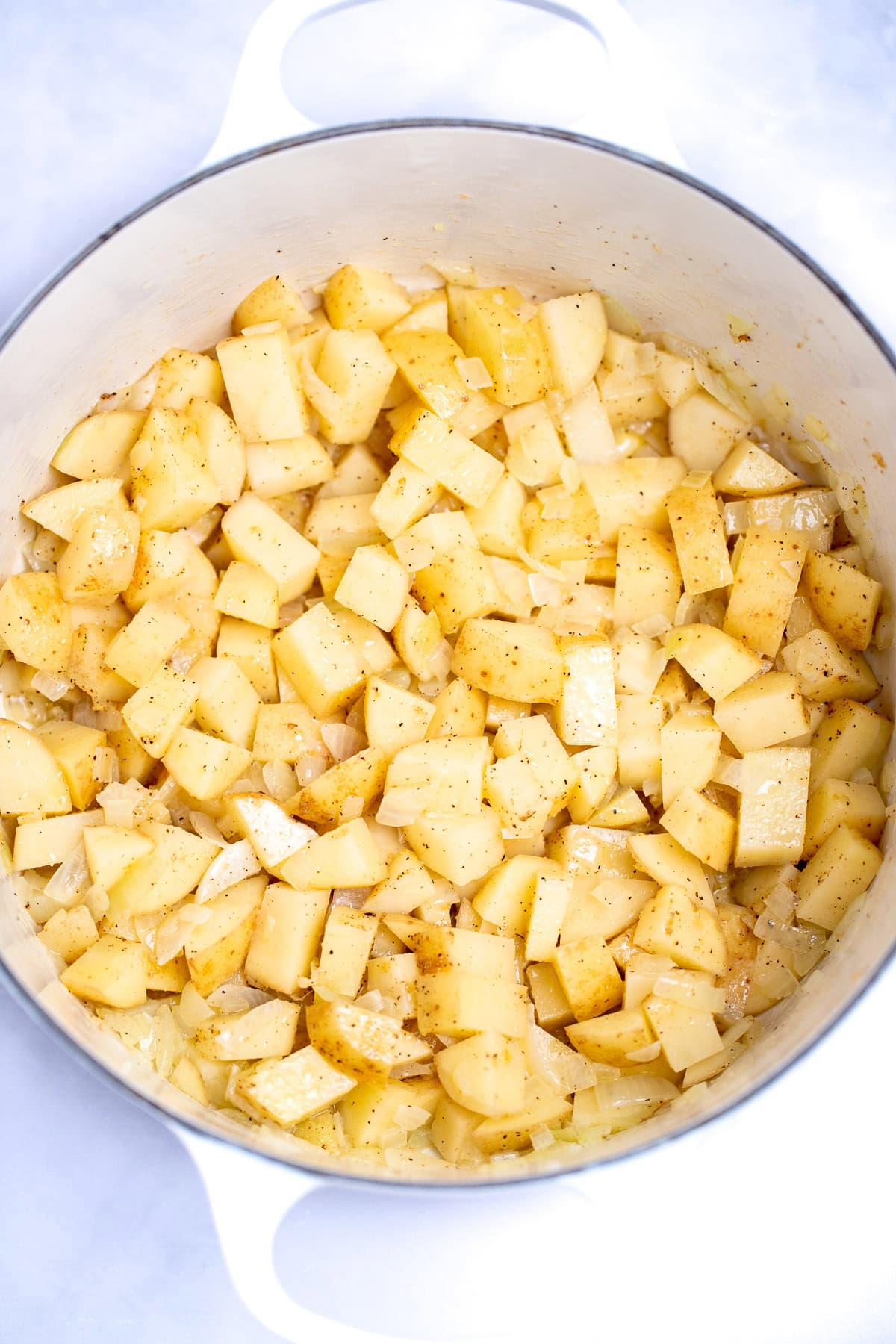 A dutch oven with sautéd and seasoned potatoes and onions.