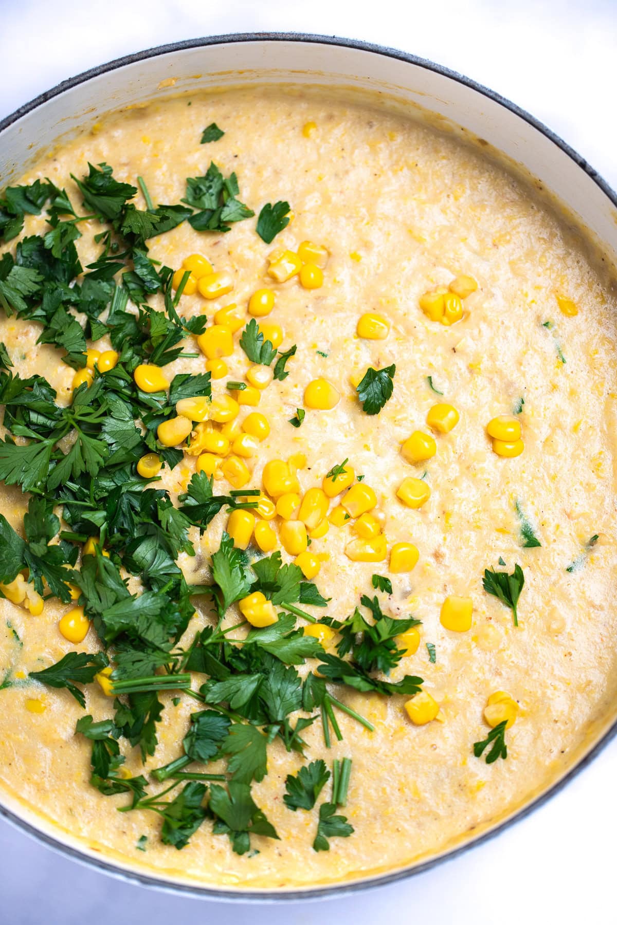 A dutch oven of crab and corn chowder topped with corn kernels and fresh parsley.