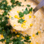 A dutch oven of crab and corn chowder topped with corn kernels and fresh parsley, with a ladle lifting some chowder up.