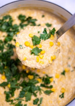 A dutch oven of crab and corn chowder topped with corn kernels and fresh parsley, with a ladle lifting some chowder up.