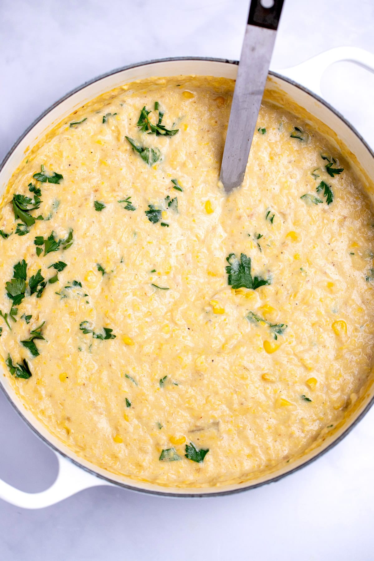 A dutch oven of crab and corn chowder topped with fresh parsley, with a ladle resting in the chowder.