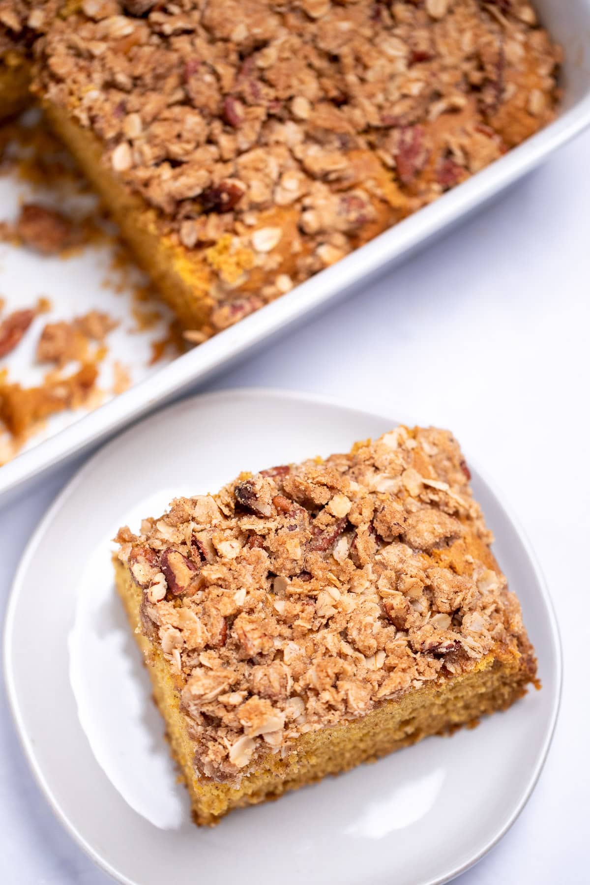 A piece of coffee cake on a plate next to the baking dish with more cake in it.
