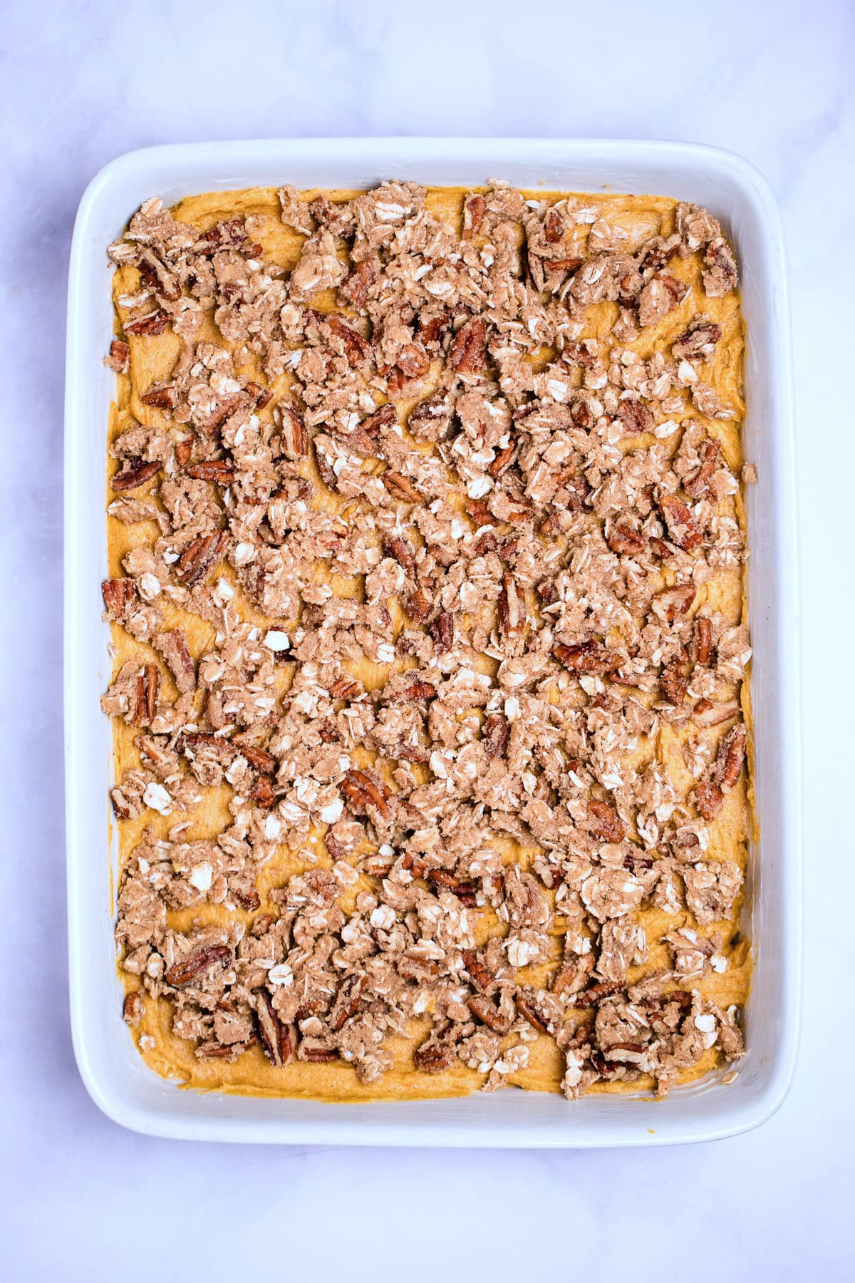 A baking dish with cake batter topped with the streusel topping before being baked.