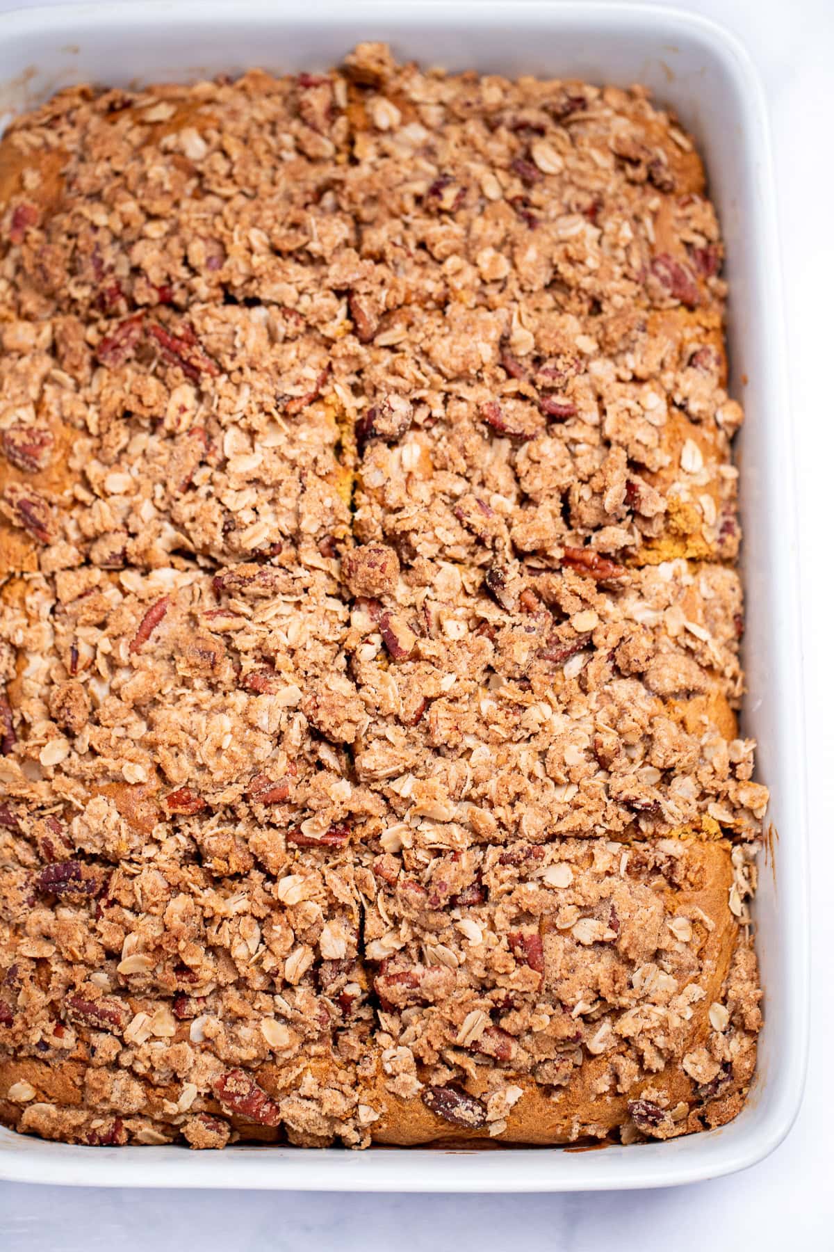 A baking dish with pumpkin coffee cake topped with streusel topping cut into 8 pieces.