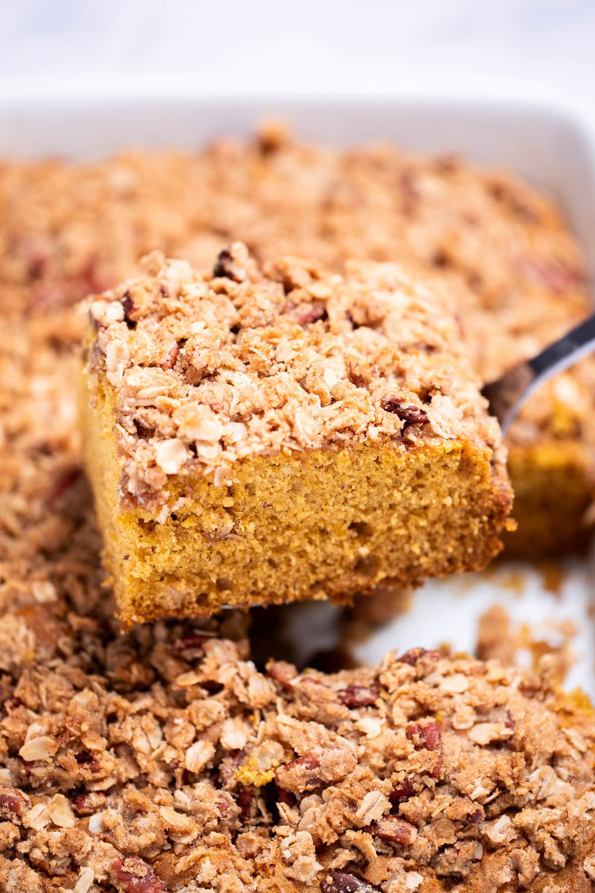 A spatula lifting a piece of pumpkin coffee cake out of the baking dish.