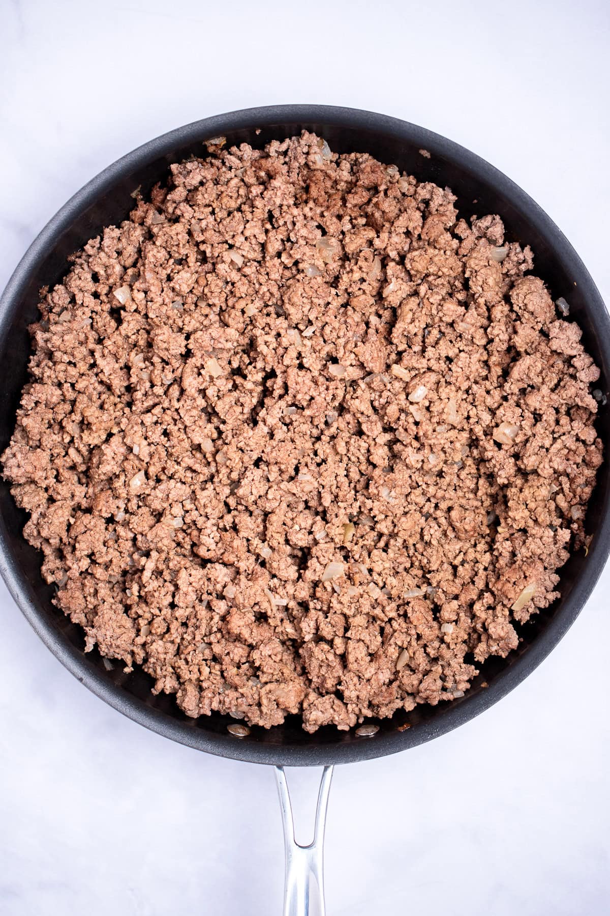 Ground beef and onion in a frying pan after being browned.