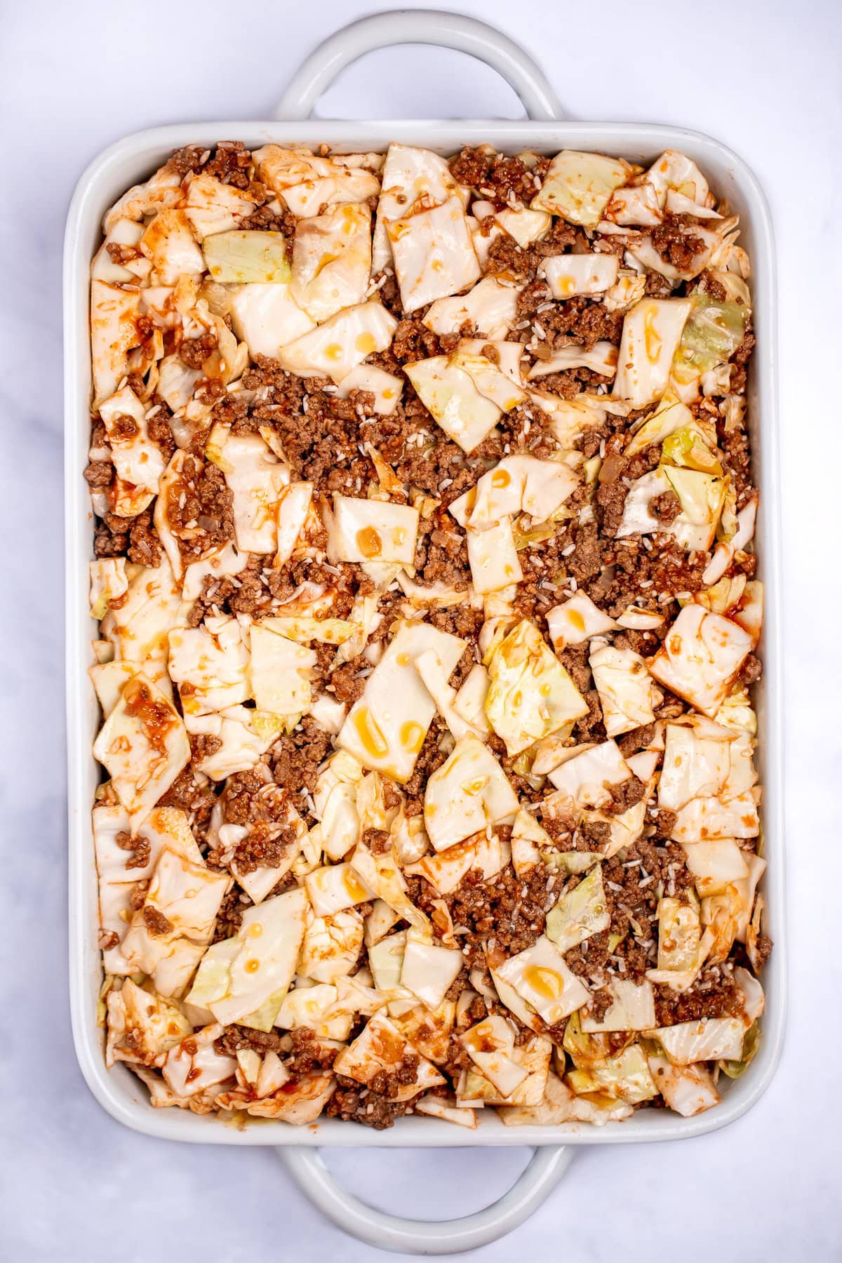 A baking dish with cabbage, ground beef, and tomato sauce mixed together before being cooked.