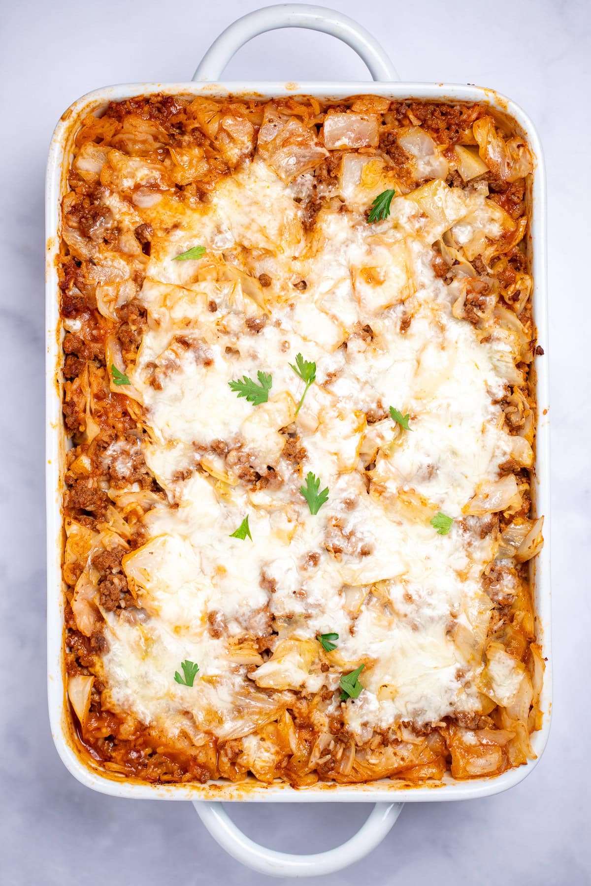 A casserole dish with Cabbage Roll Casserole topped with mozzarella cheese and fresh parsley before being served.