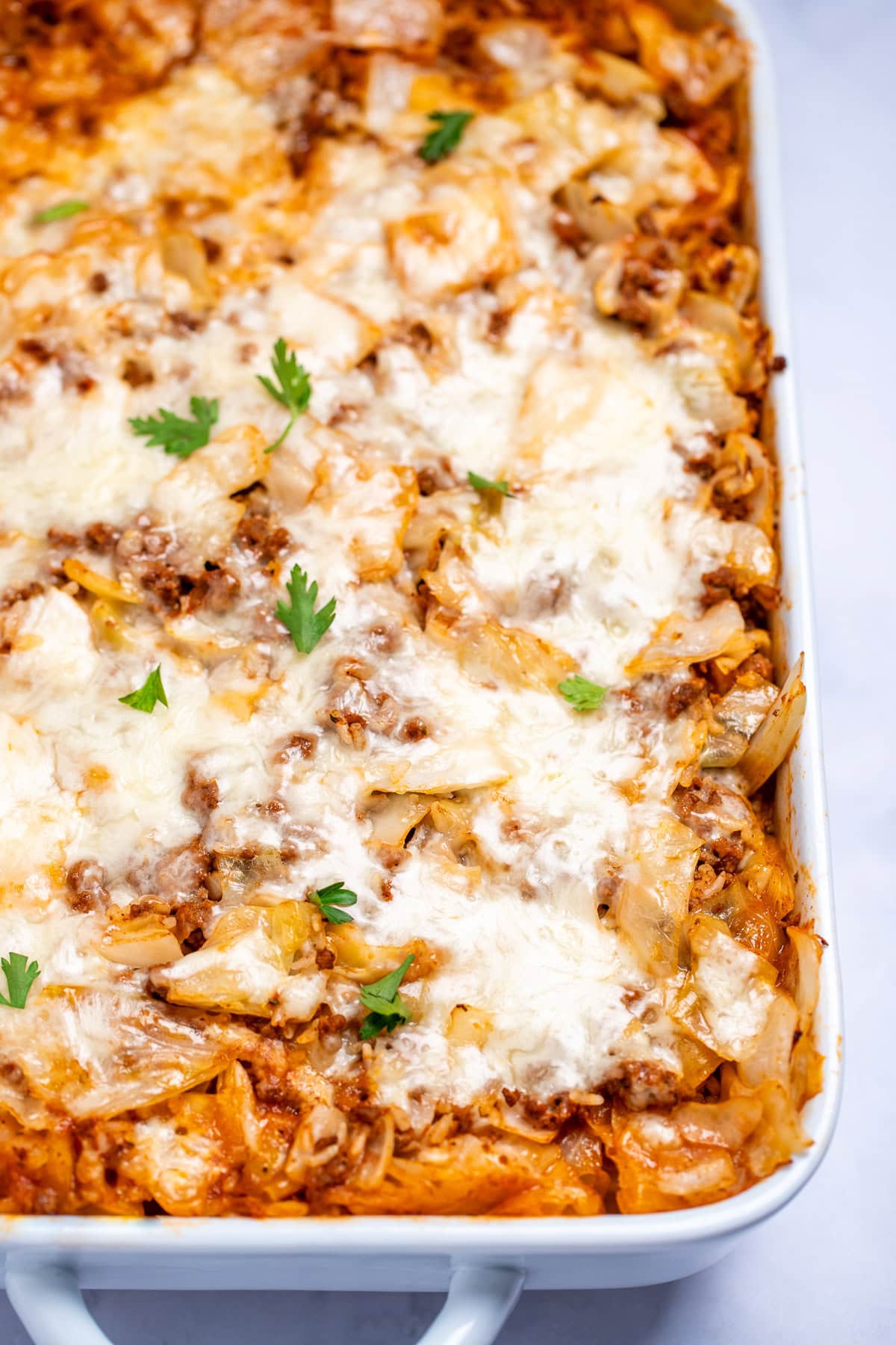 A casserole dish with Cabbage Roll Casserole topped with mozzarella cheese and fresh parsley before being served.