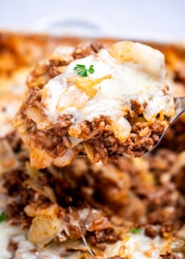 A spatula lifting some cabbage roll casserole out of a baking dish, topped with fresh parsley.